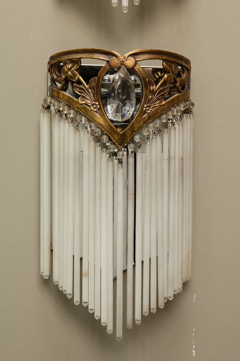 These French wall sconces date from the turn of the century. The open work bronze tone metal frame is embellished with a large, clear, faceted crystal and supports several dangling glass rods in graduated lengths. Each sconce has two light sockets