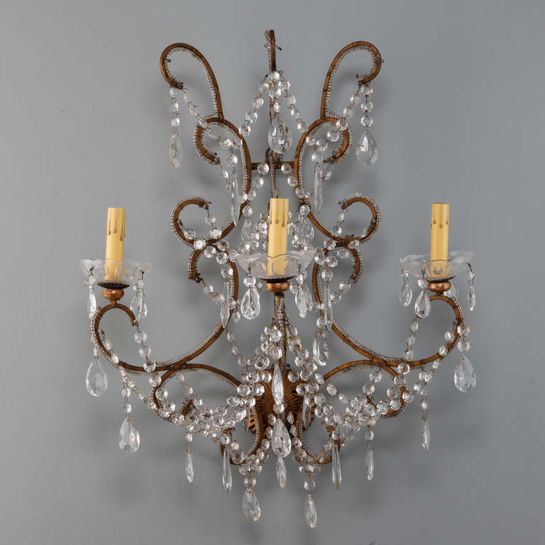 This circa 1920s French wall sconce with a gilded and scrolled iron frame and three candle style lights is draped with strands of clear crystal beads and several large tear drop faceted crystals. New wiring for US electrical standards.