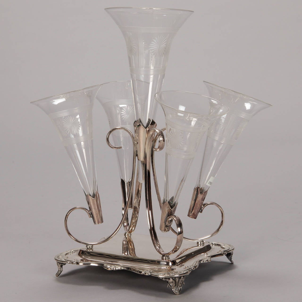 Circa 1890s silver plate five trumpet epergne found in England.  The decorative silver plate footed base has foliate details on the border and a center platform where curvy, scrolled holders are set. Four trumpets surround a taller center vessel.