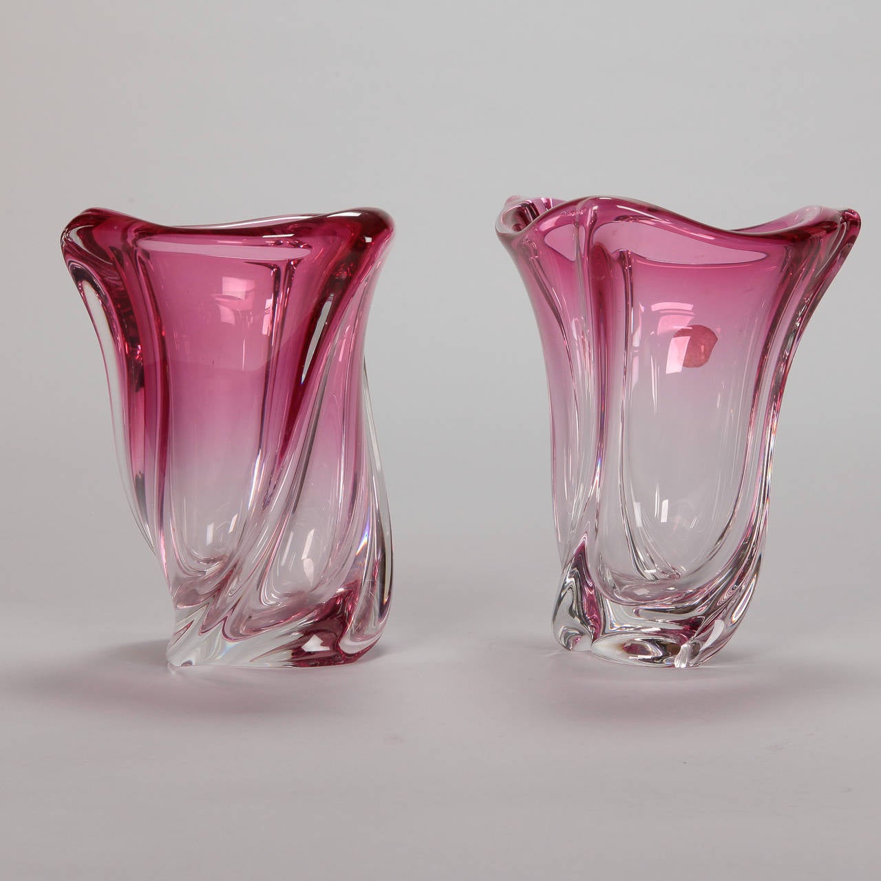 Circa 1960s pair of heavy glass vases by famed Belgian manufacturer Val Saint Lambert. Original label attached. Abstract tulip shaped vessels with ridged sides and a rich rose pink shade with most saturated color at the top, fading to clear at the