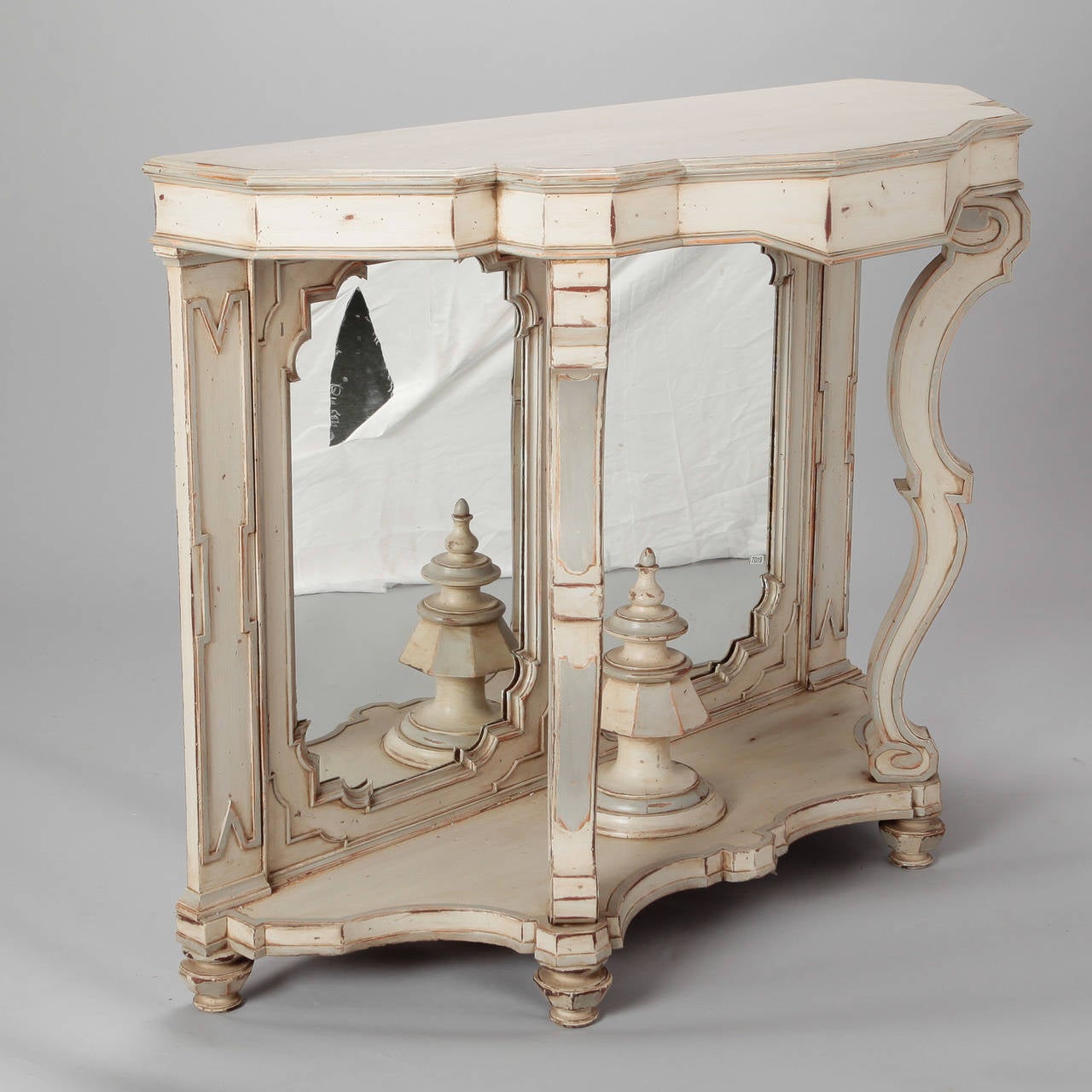 Circa 1900 Italian wood console with creamy antique white painted finish. Curved legs rest on a footed base with a double mirrored back and large, turned center finial.