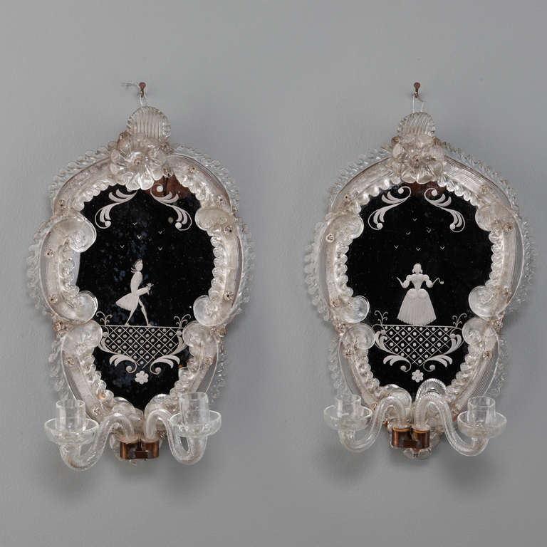 Pair of circa 1940s two arm sconces with mirror backs and clear classic-Venetian style glass frames. Mirrors have etched figures; one depicts a man, the other a woman. Sold and priced as a pair.  For use with candles only, cannot be wired.