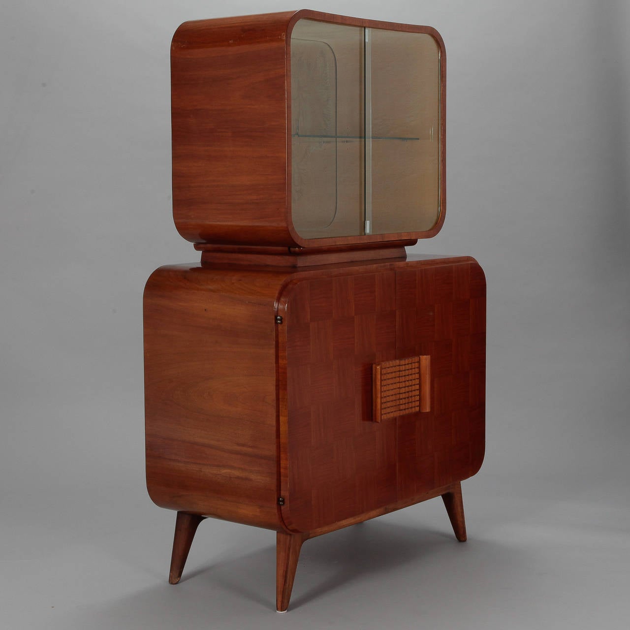 Circa 1944 bar cabinet or vitrine designed by Jindrich Halabala and manufactured by Czech Republic company UP Zavody. Checkerboard style veneer surface, top compartment has sliding glass doors and single glass shelf, bottom compartment has two