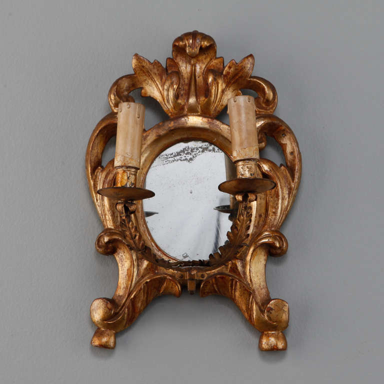 Circa 1890s pair of gild wood sconces have round mirror backs in beautifully carved and crested gild wood frames and brass candle arms. These sconces are NOT electrified. For an additional charge, we can have this pair of sconces wired for electric