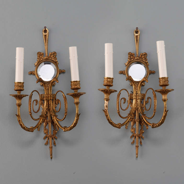 Circa 1900 gilded bronze French two light sconces with scrolled arms, candle style lights and back plates accented with rounded, beveled mirrors topped with ribbon style bows. New wiring for US electrical standards.
