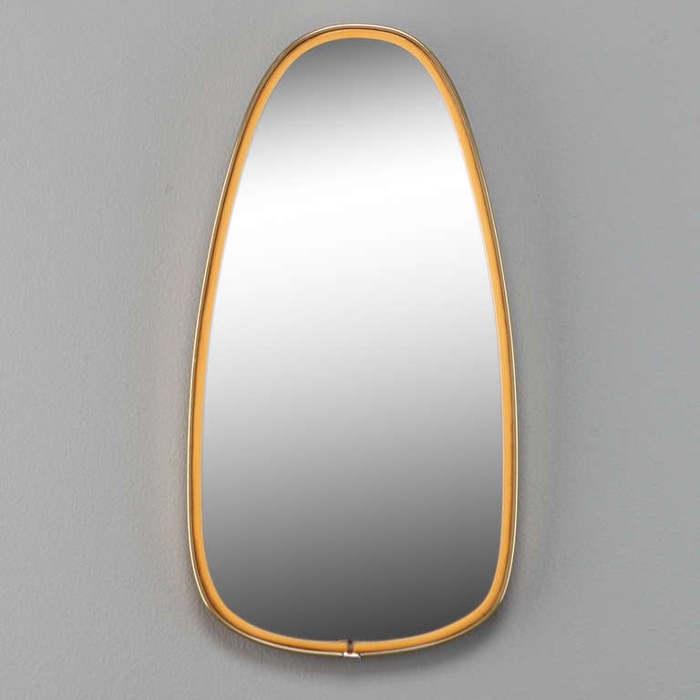 Circa 1960s Italian ovoid form mirror with a minimalist brass and yellow enamel frame in the style of Gio Ponti.