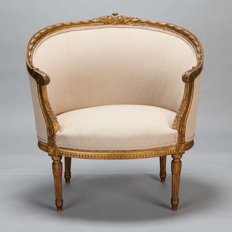 Circa 1910 French arm chair in classic Louis XVI style with curved, rounded back, carved and gilded frame, reeded legs. New upholstery in a natural colored linen with double welting. 