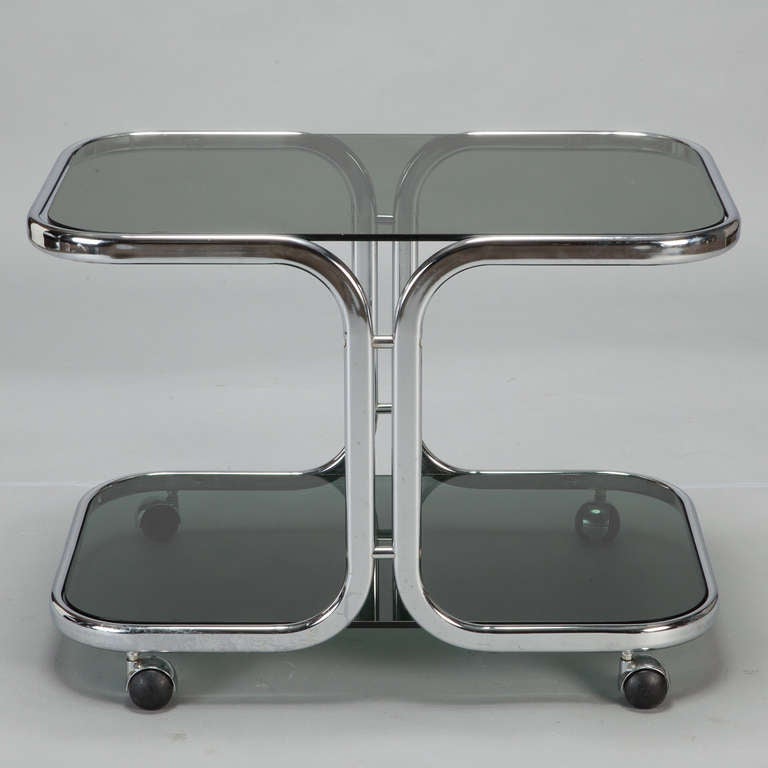 Circa 1960s trolley has a flat bar chrome frame with two black glass shelves. Chrome case casters with black rubber wheels. Use this versatile piece as a side table or small serving trolley. 
