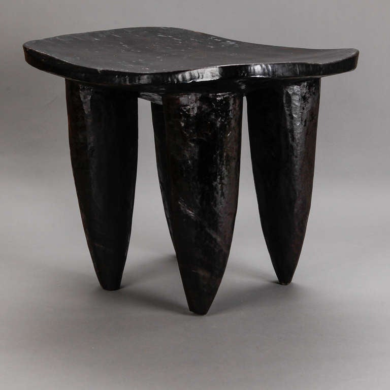 Circa 1970s hand crafted stool or table made by an artisan from the Senufo tribe residing in Africa’s Ivory Coast. This hand carved piece is made of a dense hardwood with a dark stain and features a slightly curved surface and distinct, thick,