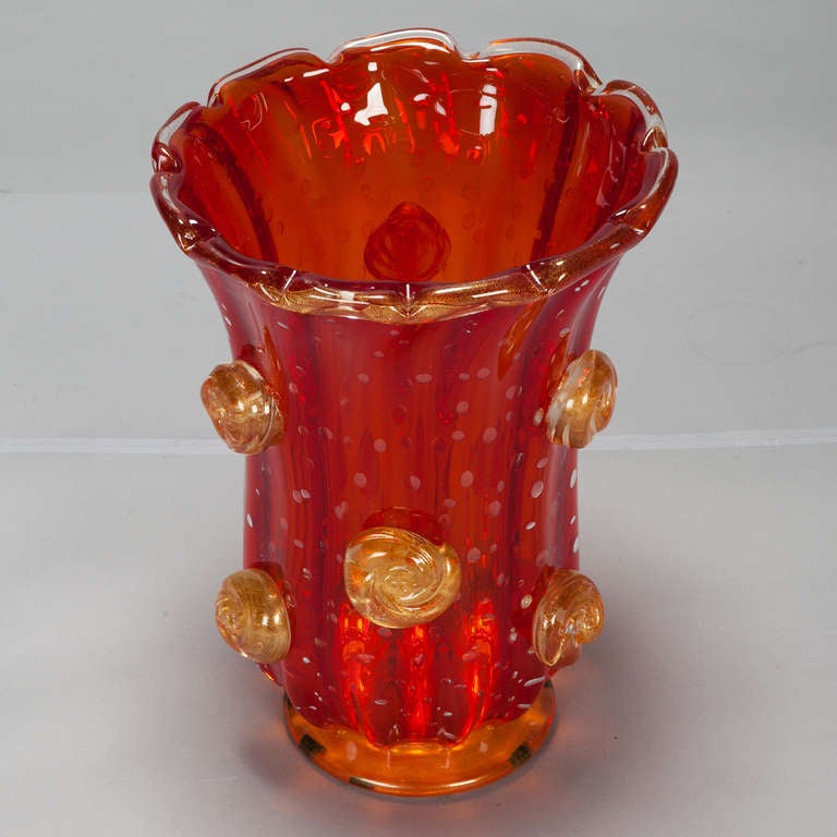 Circa 1960s red Murano glass vase has a ribbed body with applied gold knot-shaped embellishments and a scalloped rim. Engraved signature on the bottom - can't make out the name. 