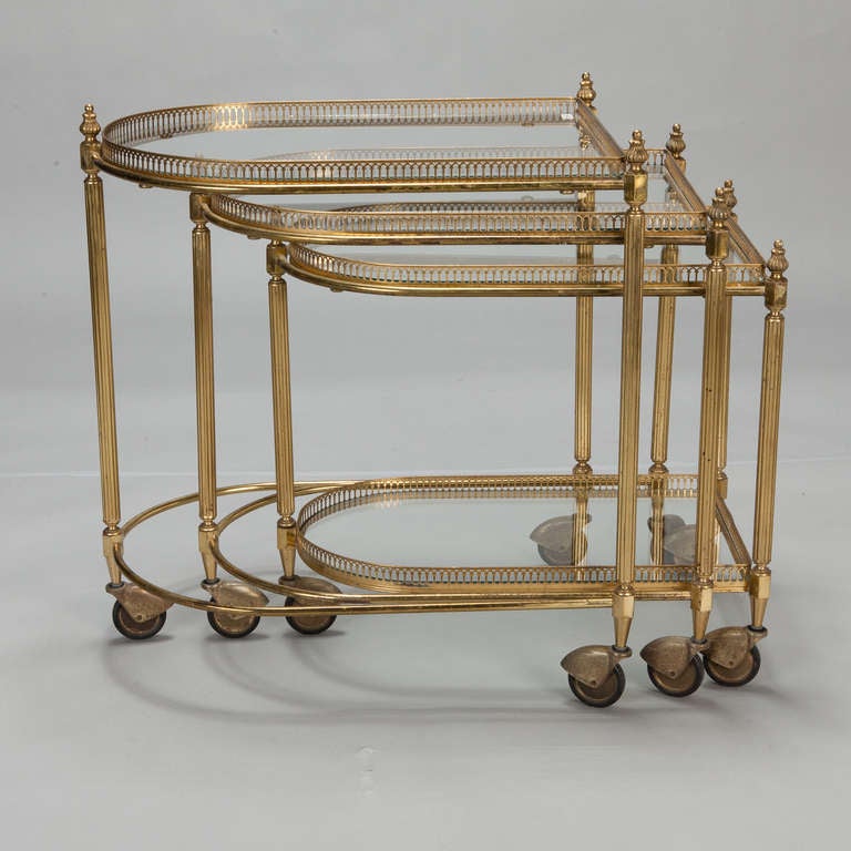 Circa 1940s set of nesting tables on casters have brass frames with reeded legs, pierced galleries and glass table tops. 