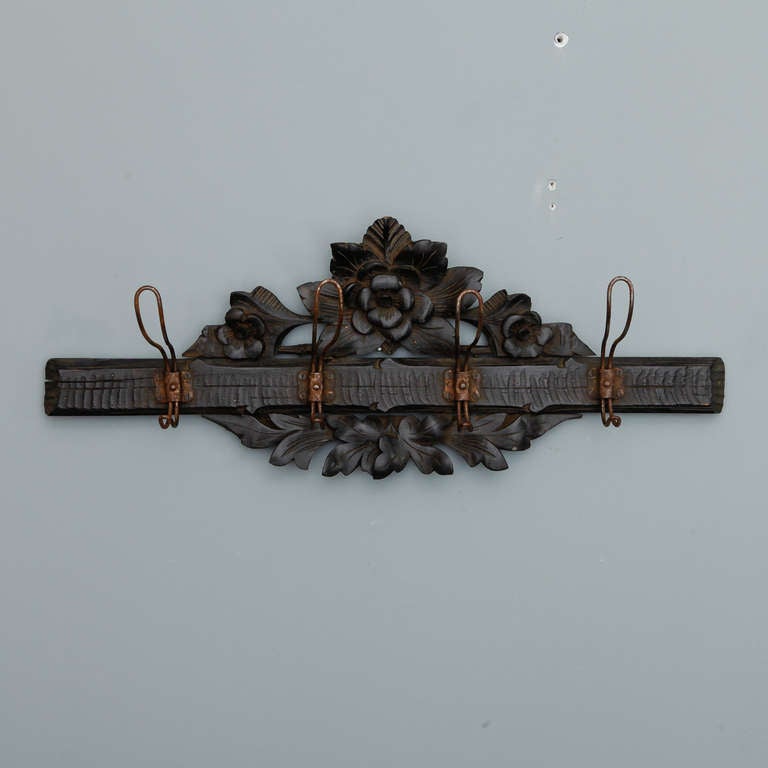 Circa 1900 hand carved dark wood wall mounted coat rack with beautifully rendered open work floral crest and four metal hooks.