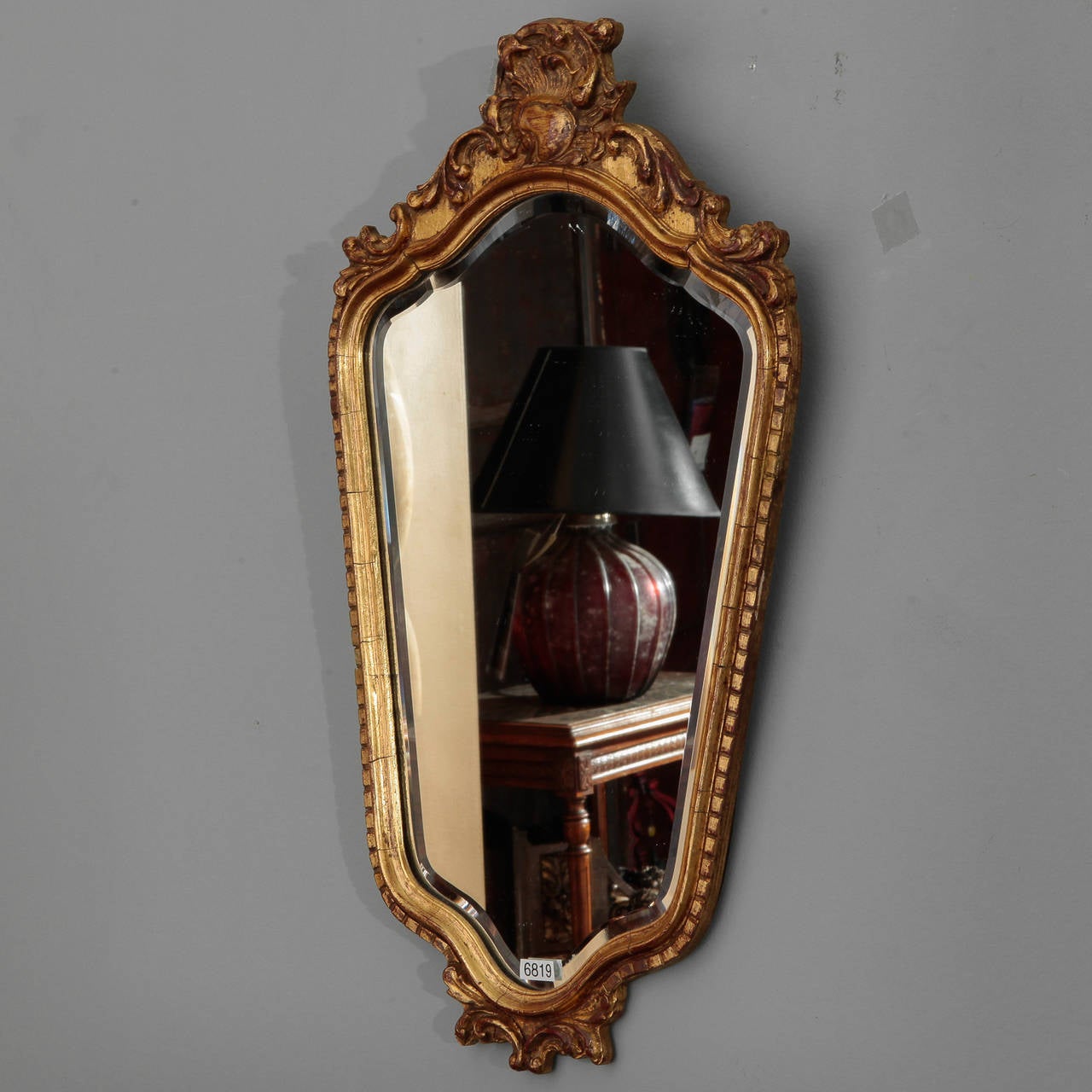 French shield shaped beveled edge mirror with wood and gesso frame in dark gilt finish and foliate crown, circa 1930s.  Actual Mirror Size:  18.25” h x 11.75” w