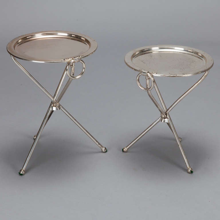 These circa 1930s silver plated end tables have round tops, ring shaped side handles and tripod stands. Measurements shown are for the larger table. Smaller table measures 14” high x 12” diameter.