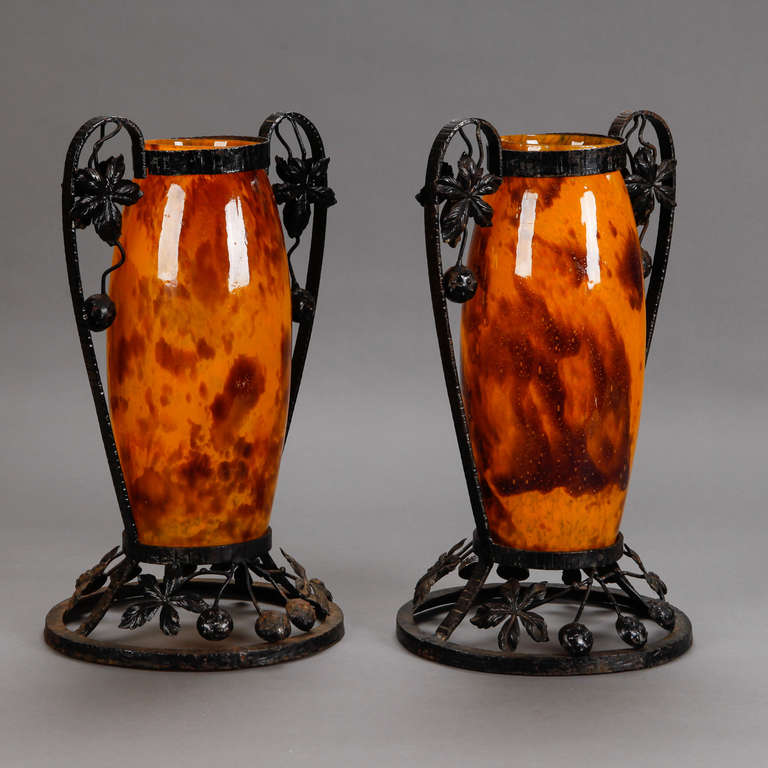 Pair of tall French art glass vases in warm tortoise and amber tone with black iron surrounds with large, curved handles and open work circular pedestal base with leaves and berries, circa 1930. Etched signature (see detail photo) Delatte Nancy.