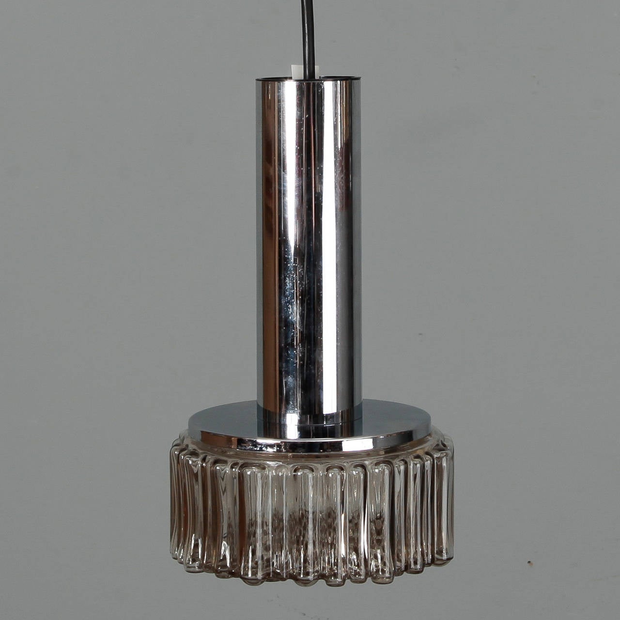 Circa 1960s German hanging pendant light fixture with a textured clear molded glass globe and cylindrical chrome shaft suspended from a black wire. We have several of these fixtures available and they can hung individually or as a group. New wiring