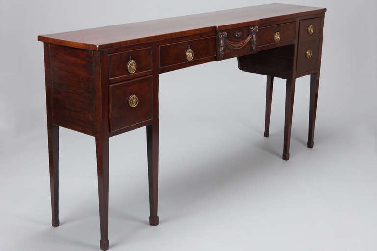 Circa 1880s English mahogany breakfront server has six legs, six drawers, brass hardware and a carved garland embellishment. Original depth has been reduced by professional cabinet makers to make this a more versatile size.