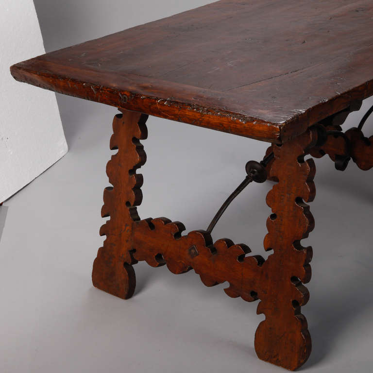 Circa 1880s Spanish dark oak table has a smoothly worn top with banded ends, three trestle legs with carved edges and a black iron stretcher.