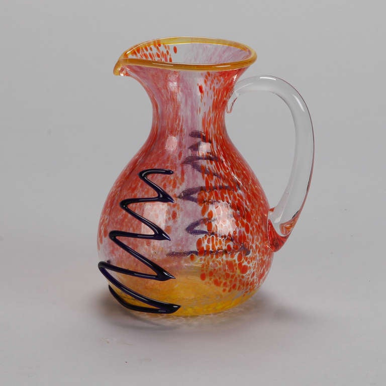 Circa 1980s colorful glass pitcher by glass master Mario Badioli in shades of red and gold with applied purple designs. Signed by the artist.
