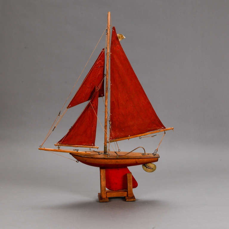 Circa 1900 English wooden pond boat with three red cloth sails, brass tiller and hardware and original wooden display stand.