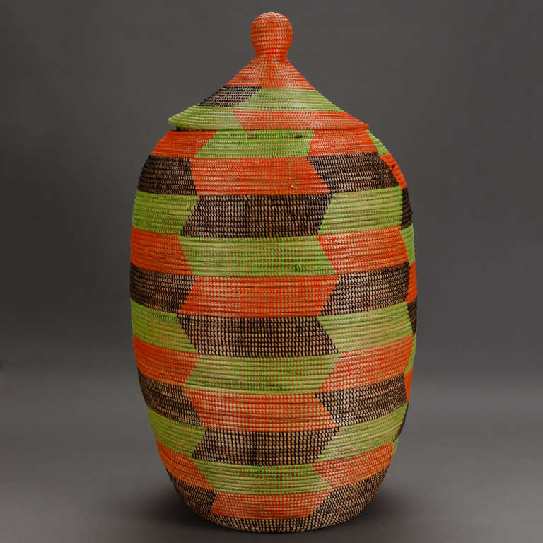 Circa 2000 tall standing hand woven floor basket with fitted lid from Senegal, West Africa in shades of green, brown and orange.
