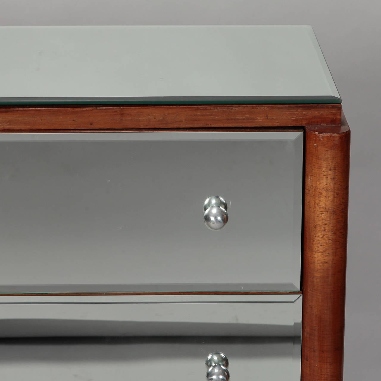 Circa 1930s commode or small chest of three drawers with walnut frame and mirrored drawer fronts, top and sides. Curved apron and tapered legs with brass capped feet. Found in England - maker unknown. This piece would be great next to a bed or sofa.