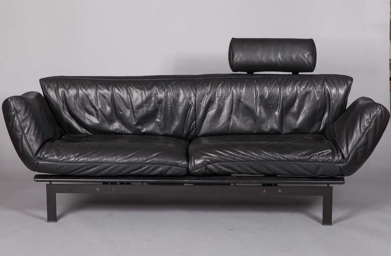 Circa 1970s black leather sofa with steel frame by Swiss maker De Sede. Sides can be folded up as arms, left flat to elongate sofa or swivel around to the front as a recliner. Removable headrest adds 8