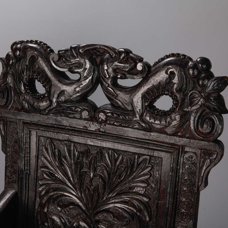 Circa 1830s pair of dramatic English dark oak arm chairs with pair of elaborately carved Chinese style dragons on the crest. Decorative scrolled arm, turned details on the spreaders and legs with a back rest carved with leaf form design in relief.
