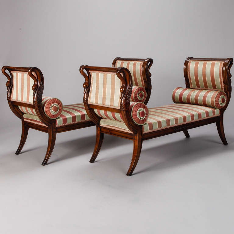 Pair of upholstered French benches in Classic Empire style with carved swan details on the high, curved sides and tapered, saber style legs, circa 1930s. Older striped upholstery and round bolster pillows. Seats are 12” high and 16.5” deep. Sold and