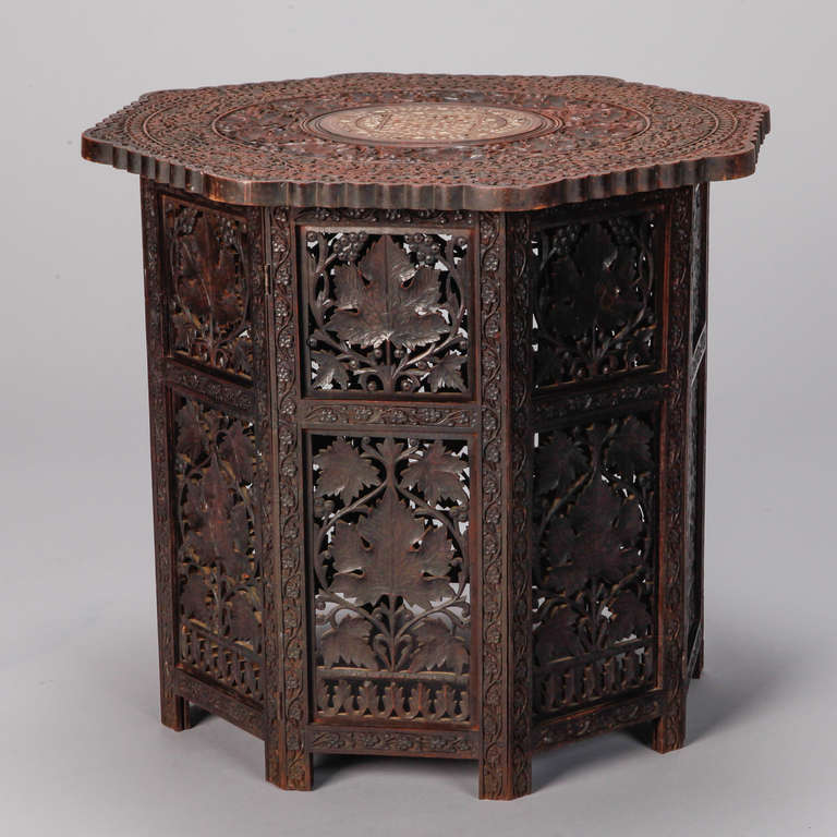 Circa 1920s dark wood Moroccan style table with delicate, open work carved leaf design on sides and decorative bone inlay on the top. Base is comprised of eight side panels that are hinged and can be folded flat with top lifted off for easy storage