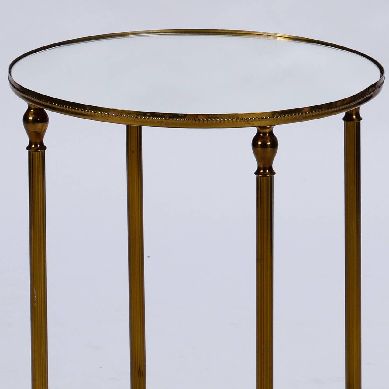 Found in France, this circa 1960s small, round neoclassical styled side table has a brass frame and mirrored top. Excellent vintage condition with some patina to brass surface.