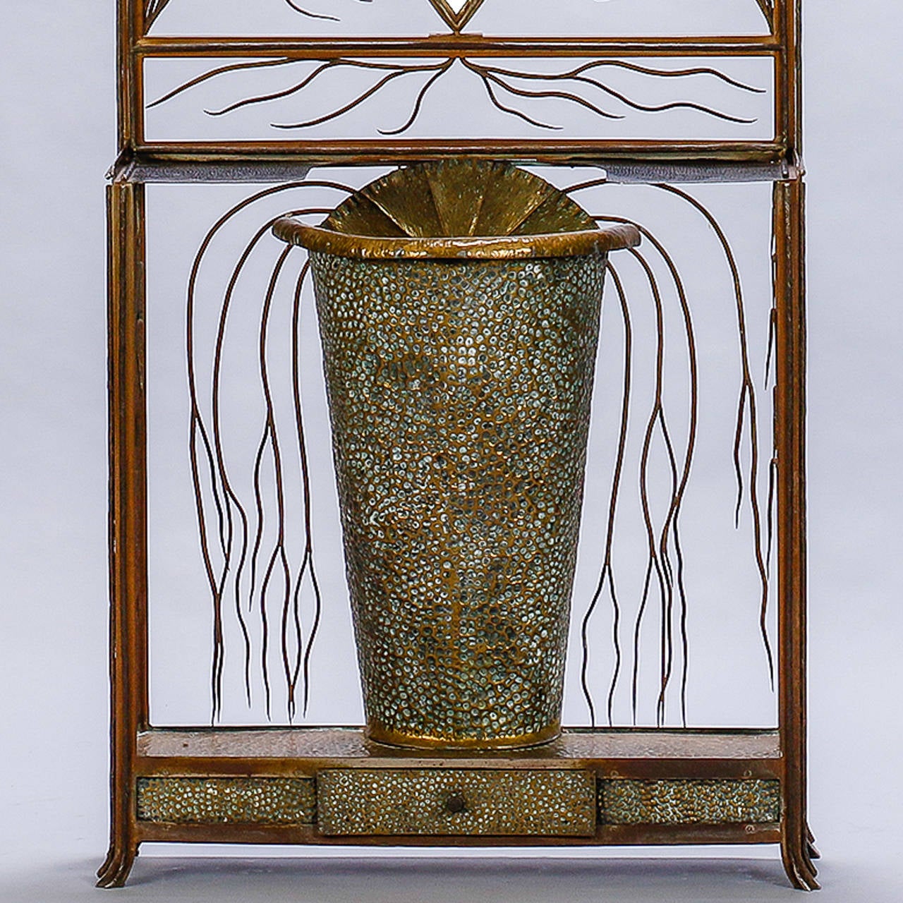 Found in France, this Art Deco era hall tree and umbrella stand has a sculptural quality with hammered brass and decorative, detailed work with slender, curved strands forming a crest and framing the beveled ovoid mirror and umbrella holder.