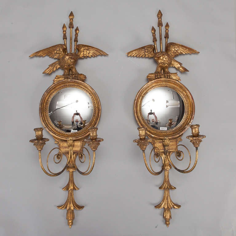 Circa 1940s pair of gild wood candle sconces feature two candle arms each with round mirror back and large eagle and triple arrow crest. Can be electrified for additional charge. Sold and priced as a pair.