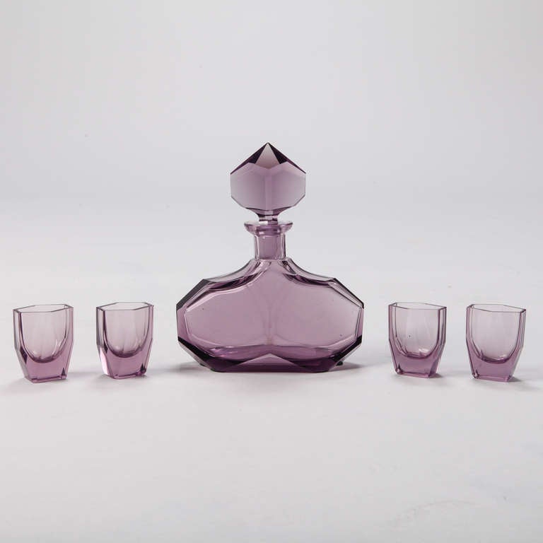 Circa 1930s Art Deco era amethyst Bohemian glass decanter with faceted sides and decorative stopper with four matching glasses. Measurements shown are for the decanter; glasses are 2.5