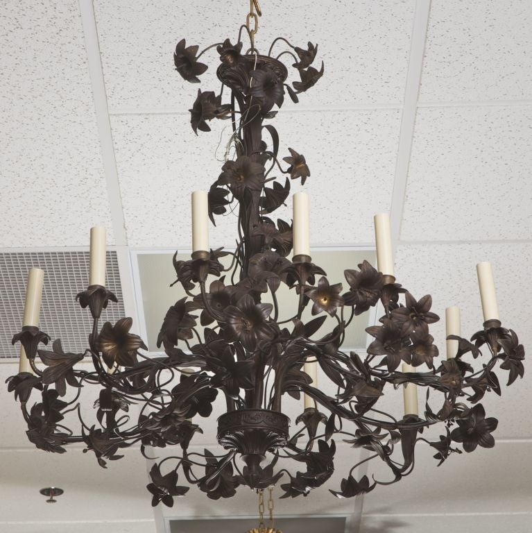 This circa 1900 French tole black finish chandelier has twelve candle style lights and a design of intertwined, elaborately rendered lillies.