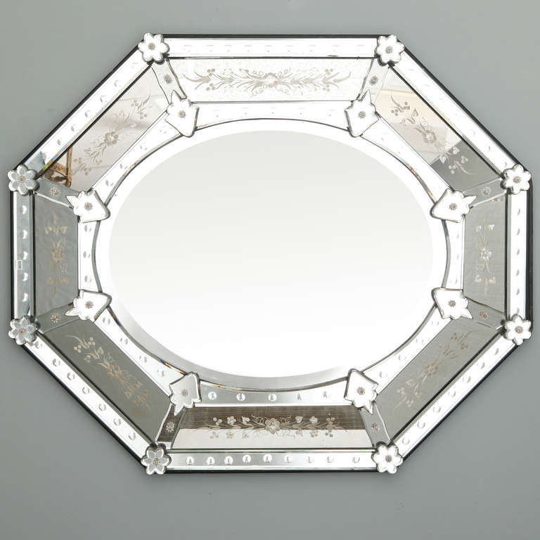 Circa 1920s Venetian mirror in elongated octagonal shape. Can be hung horizontally or vertically. Beveled edge oval center mirror framed with decorative elements that include etched floral details, glass flowers and arrow shaped fasteners.