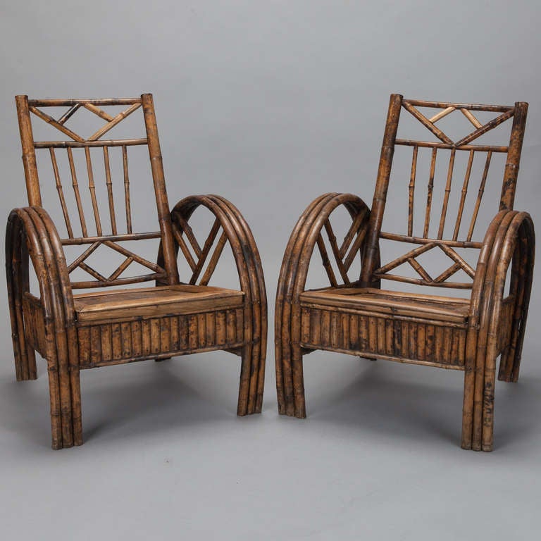 Bamboo set of two armchairs and matching occasional table from Colonial India, circa 1910. The pair of bamboo armchairs in a natural finish feature high backs with a geometric open work design and dramatically curved three strand arms and legs with