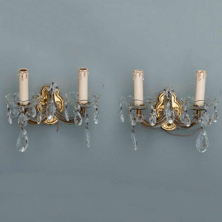 Circa 1940s classic Maria Theresa style crystal wall sconces with two arms, candle style lights and polished brass back plate. Glass bobeches and large crystal drops. Found in France. New wiring for US electrical standards.