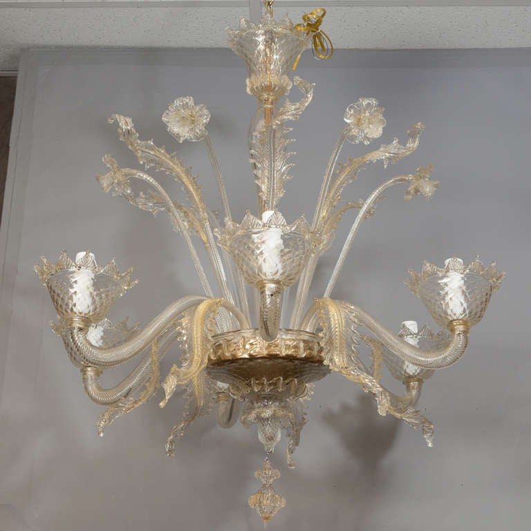 Circa 1950s six arm Venetian glass chandelier in a pale gold shade with gold inclusions. This classic daffodil chandelier has upright blooms and leaves with curled leaves between the candle arms. Bobeches and ceiling canopy have petal edges and the