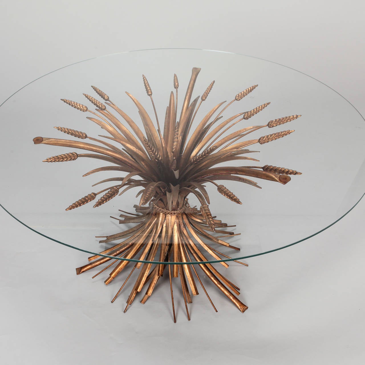 Cocktail or side table has a gilded metal base in the form of gathered wheat sheaves with a round glass table top. Found in Europe probably originates from Italy, circa 1940s.