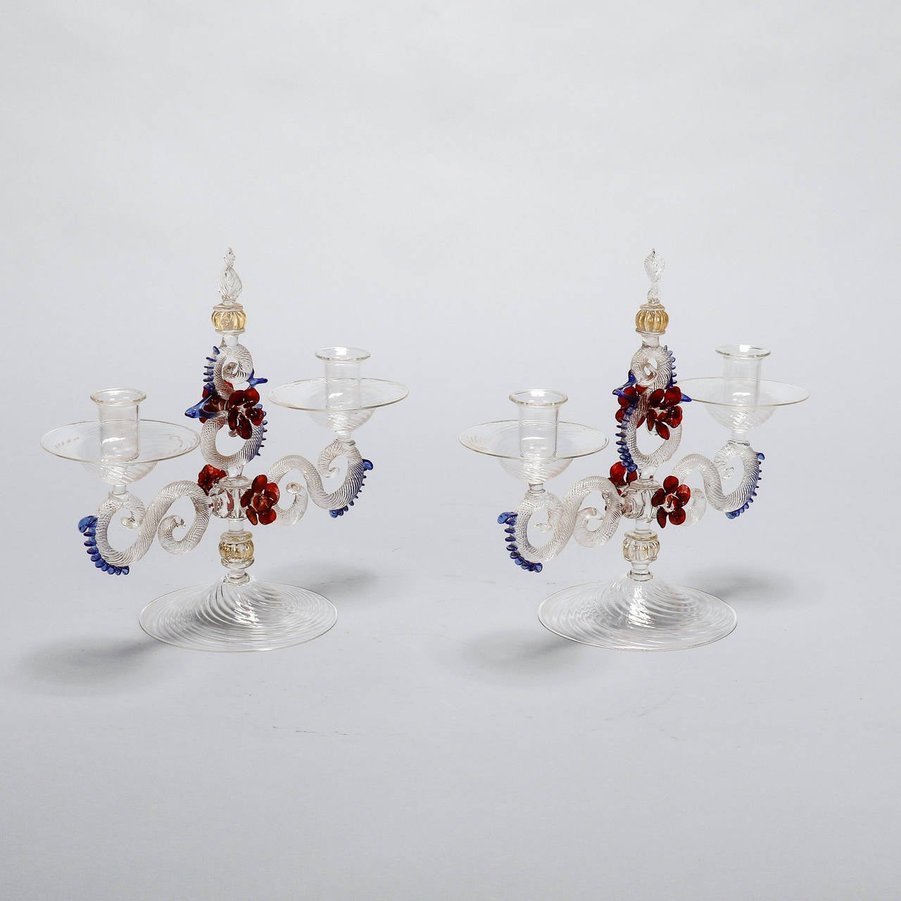 Pair of hand blown Venetian glass candlesticks with two candle cups each. Base is clear glass embellished with red flowers and blue accents. Sold and priced as a pair, circa 1900.
