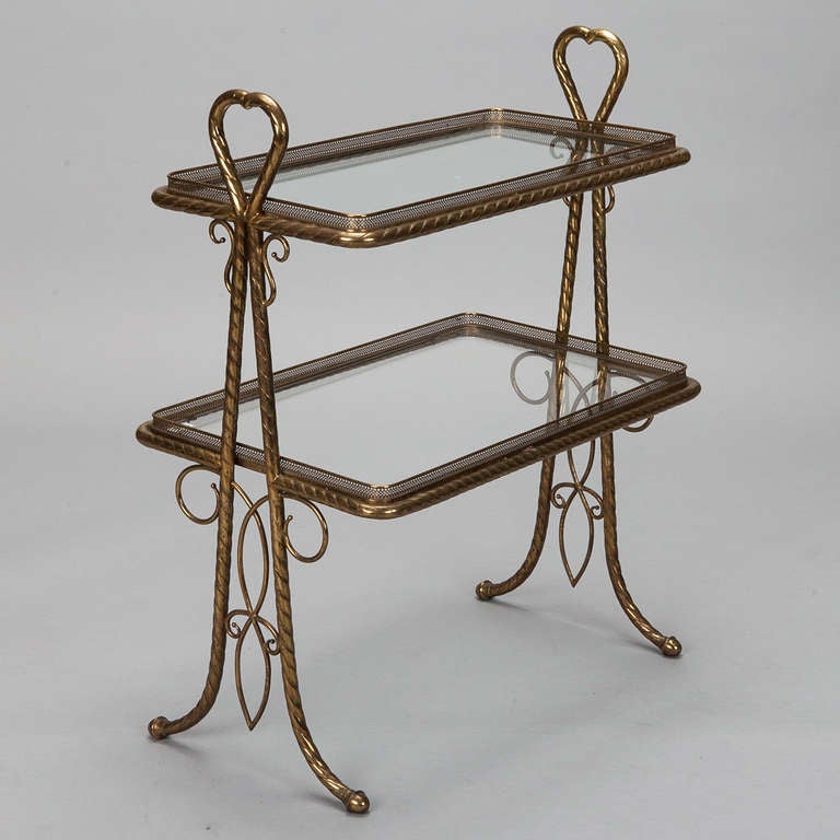 Circa 1940s Italian side table / stand has a brass frame with decorative open work scrolls at the sides and two graduated glass shelves.