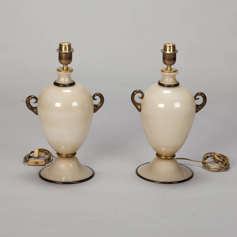 Pair of Murano glass lamps with classic amphora form bodies and pedestal base, circa 1950s. Lamp bodies in glossy shade of cream accented with black adventurine and gold glass. New wiring for US electrical standards. Sold and priced as a pair.