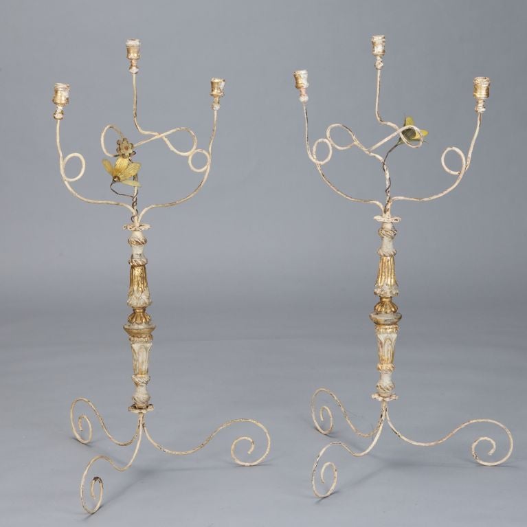 Great pair of dramatic table candelabra assembled using 19th century antique elements. Gilded, painted and carved wood base with scrolled iron tripod feet, three curved and scrolled candle arms with tole flower accent.