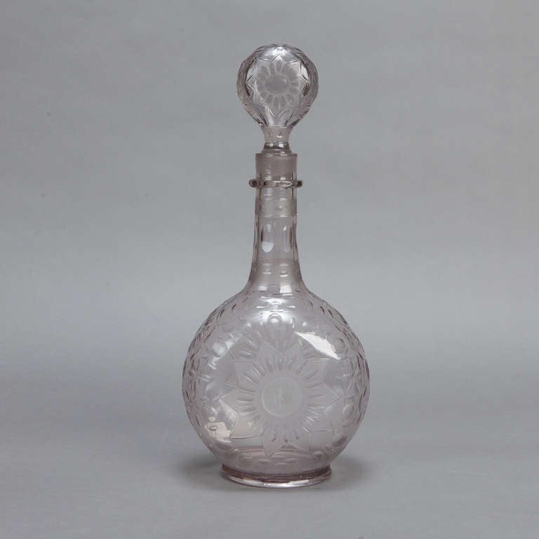Dramatic crystal decanter with an all over floral design, round body, slender neck and large, decorative round stopper.  Crystal is a very pale shade of smoke gray.
