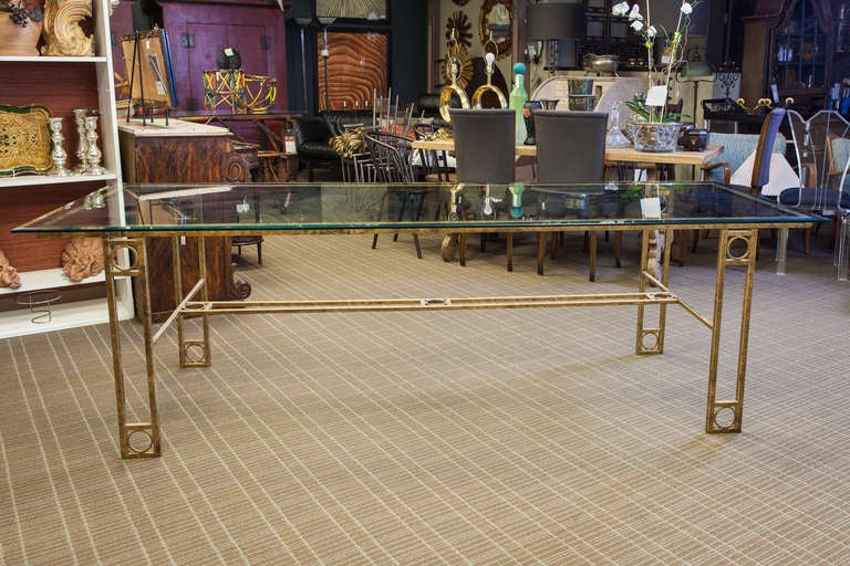 Circa 1970s European dining table has an iron base with a burnished gold finish and open work design of rectangles and circles and a beveled edge glass top.