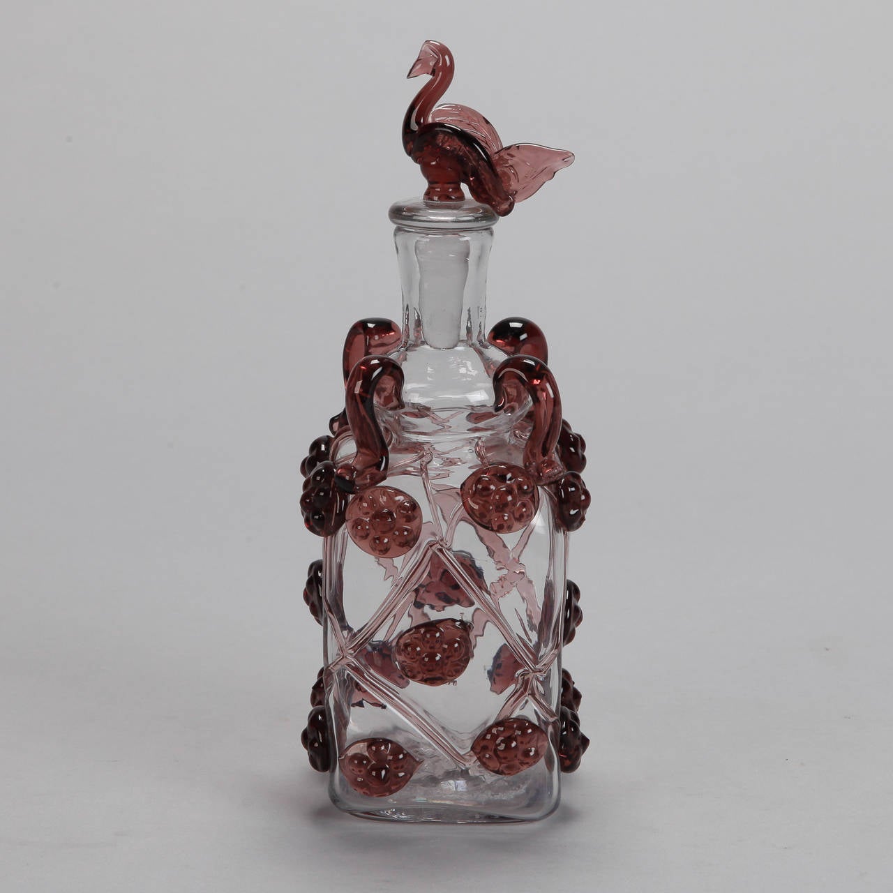 Circa 1950s clear glass decanter with plum colored applied glass decorations. Stopper has a bird form top.
