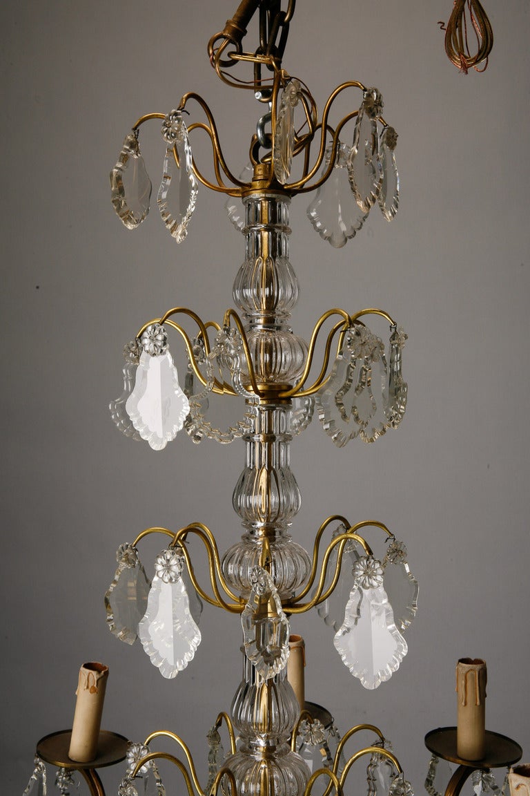 French eight-arm brass chandelier with candle style lights has decorative glass shaft and is embellished with several large cut crystal pendants and a clear crystal ball drop. New electrical wiring, circa 1920s.

No of sockets: Eight.
Socket type: