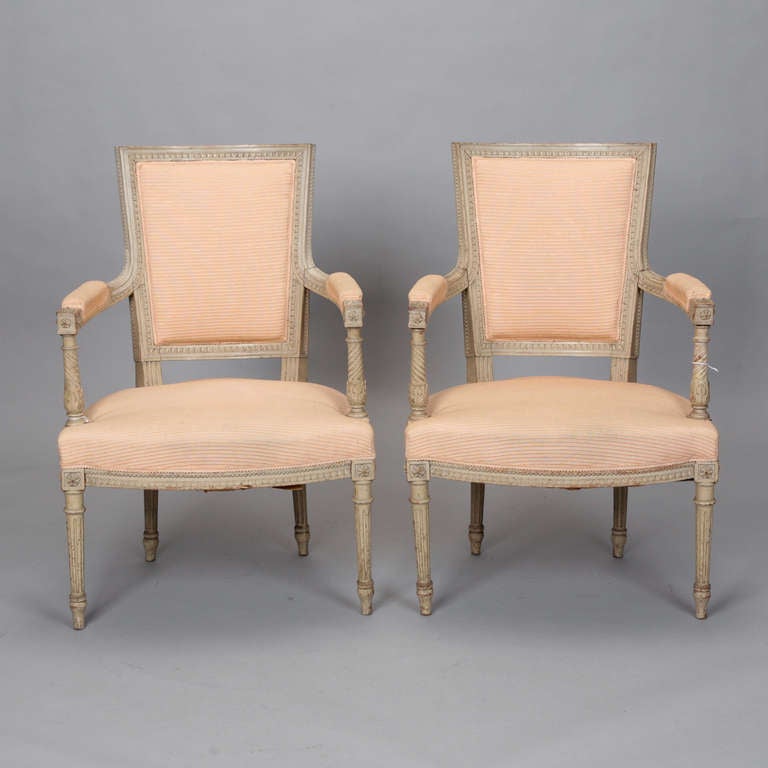Turn of the century French armchairs with class Louis XVI styled frames featuring decorative carved details on legs, arms and seat backs. New upholstery in pale apricot with subtle ribbed surface texture. Seat backs have coordinating striped fabric.