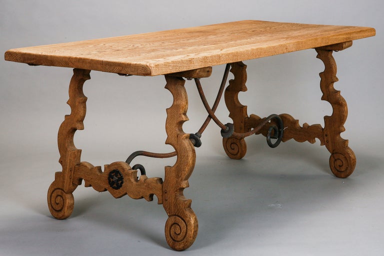 Late 19th century bleached oak Spanish dining table has criss-cross scrolled iron stretcher and decorative carved legs with scrolled feet. 